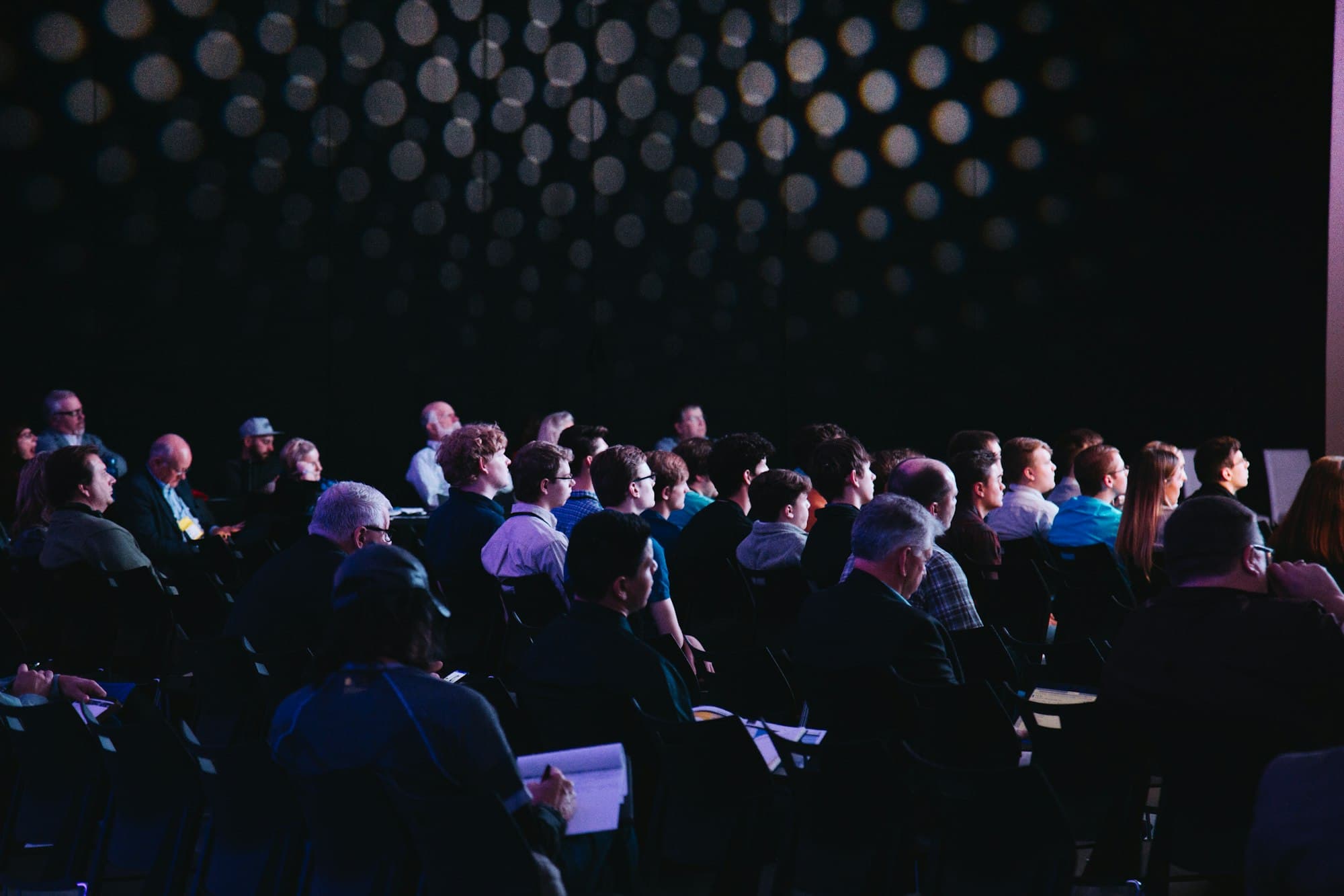 Audience seated in a darkened auditorium during a conference session.