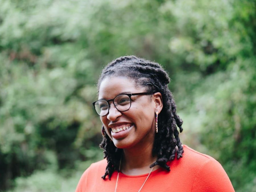 Illustrative portrait of a smiling woman with locs and glasses, used for a sample speaker profile.